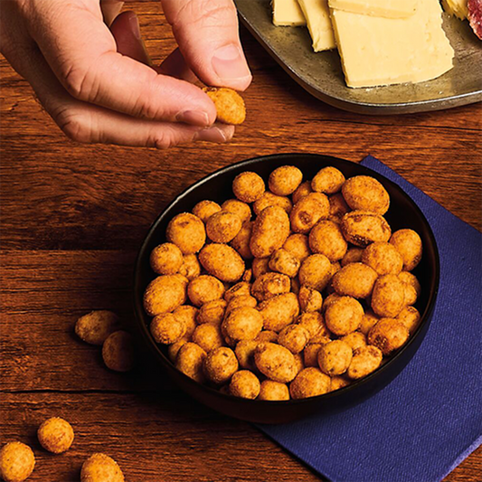 Hand picking a snack from a bowl of round, golden-brown snacks on a wooden table.